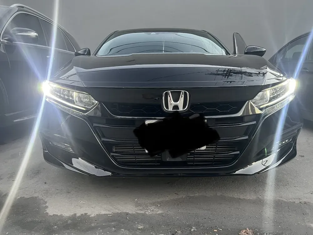 Front of a black Honda Accord sedan with its headlights on