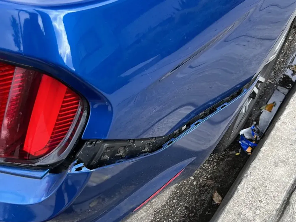 Blue Ford Mustang rear bumper cover pulled loose from the quarter panel after a collision