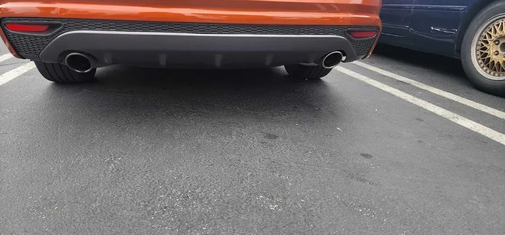 Rear bumper and dual exhaust tips of an orange car in a parking lot